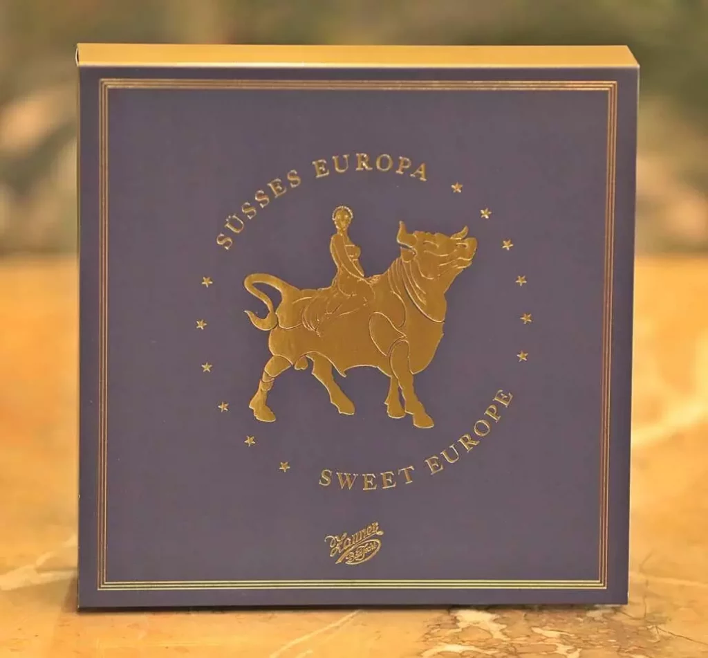 Product image with a golden background, packaging of the European cake from the Zauner Konditorei.