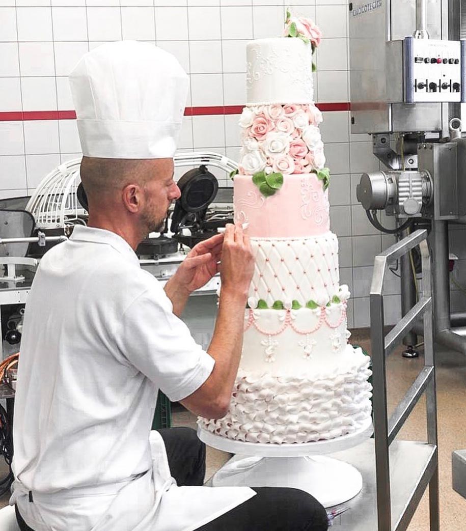 ein Meister-Konditor verziert eine 6-Stöckige Torte aufwendig mit feinen Linien.