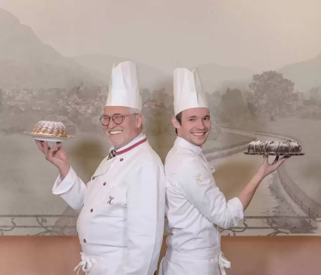 Josef and Philipp Zauner stand back to back, smile into the camera and each hold up a cake.